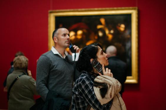 Man and woman hold dedicated audio tour device to their ears in an art gallery.