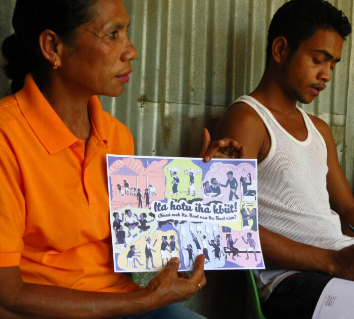 A Timorese woman shows a colourful pamphlet while sitting next to a man.