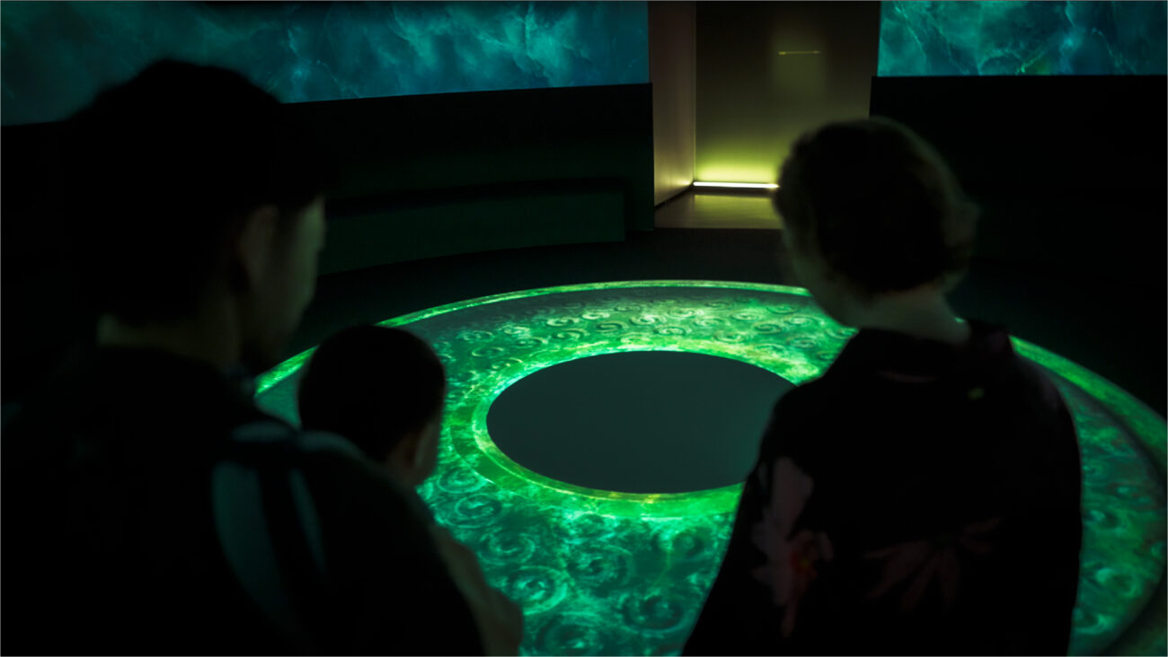 Silhouettes of young family look down at a low projection table showing a jade bi disc at WA Museum.