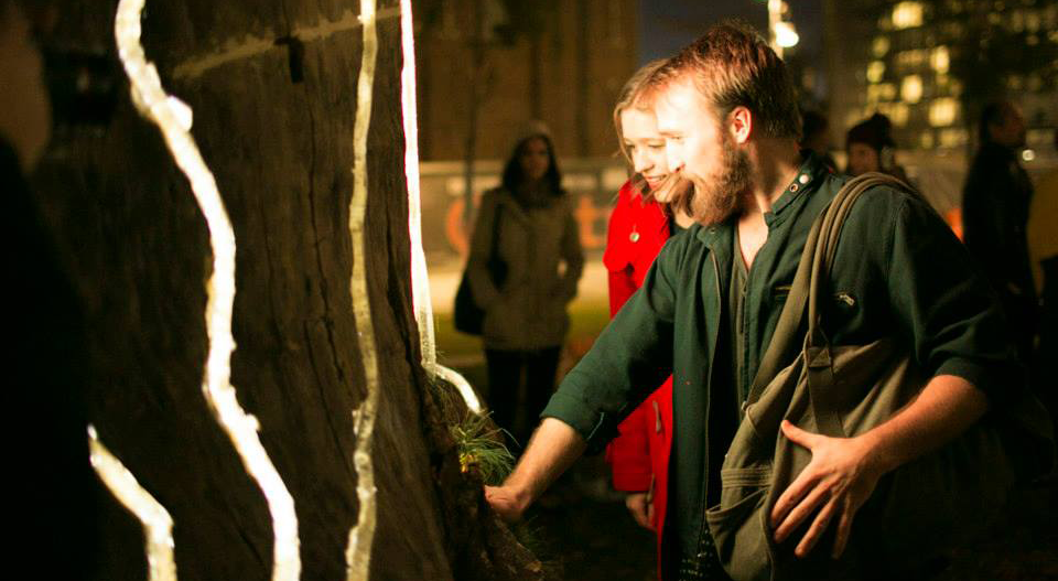 Man and woman use their heartbeat to activate light and sound show in Adobe Heart Tree interactive artwork.