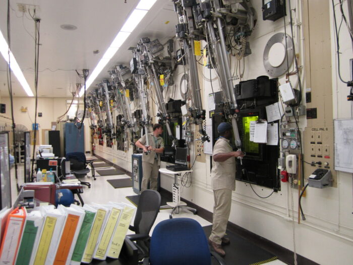 Nuclear research scientists use heavy lead windows and robotic arms to interact with a nuclear hot cell containment environment.