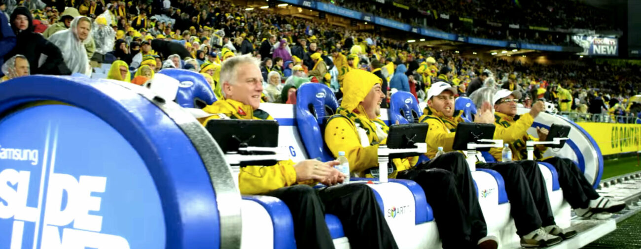 Sports fans sit on Samsung SlideLiner couch with interactive tablets to follow rugby game.