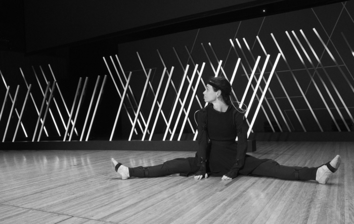 Dancer Naomi Hibberd sits on stage of the Sydney Opera House in a Rokoko motion capture suit.