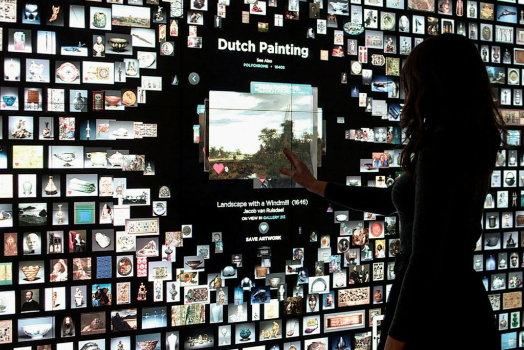 Woman interacts with information provided in the ARTLENS project through a large interactive touch screen.