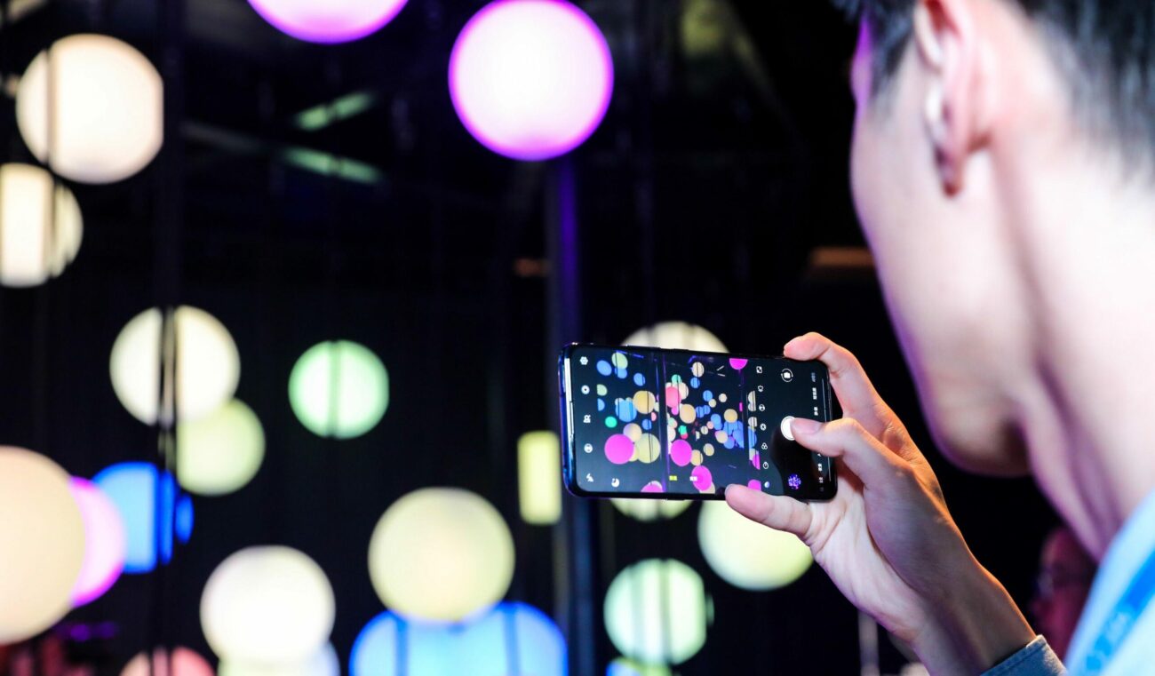 Man takes a smartphone photo of colourful, glowing light orbs in the Touching Photons creative technology experience at the vivo Lab experience centre.