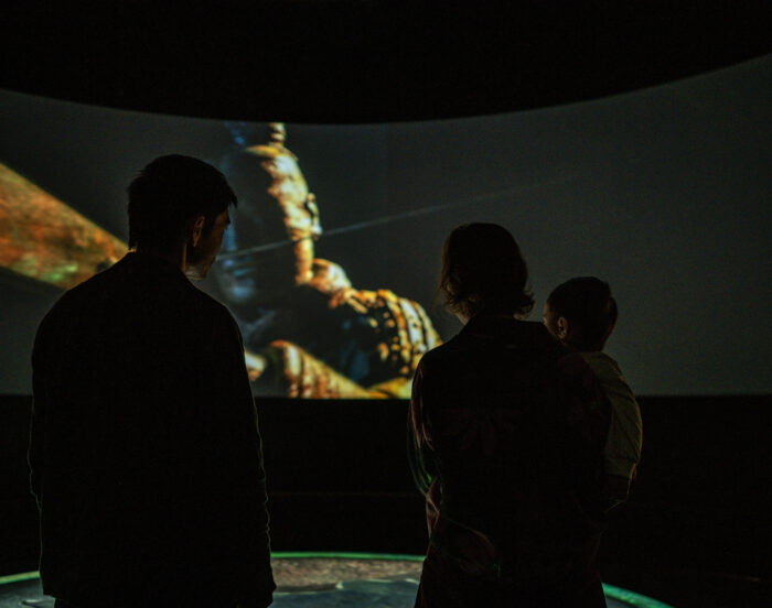 Man and woman stand facing Terracotta Warrior on wraparound projection mapping experience for Western Australia Museum.