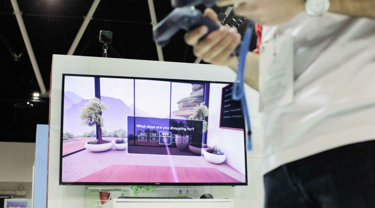 Man with virtual reality controllers stands in front of a screen showing his virtual reality experience in Adobe Future of Retail at the MAKE IT Conference in Sydney.