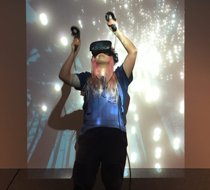 Woman uses HTC Vive virtual reality headset to interact with interactive story Kept VR in front of projection screen at the Powerhouse Museum.