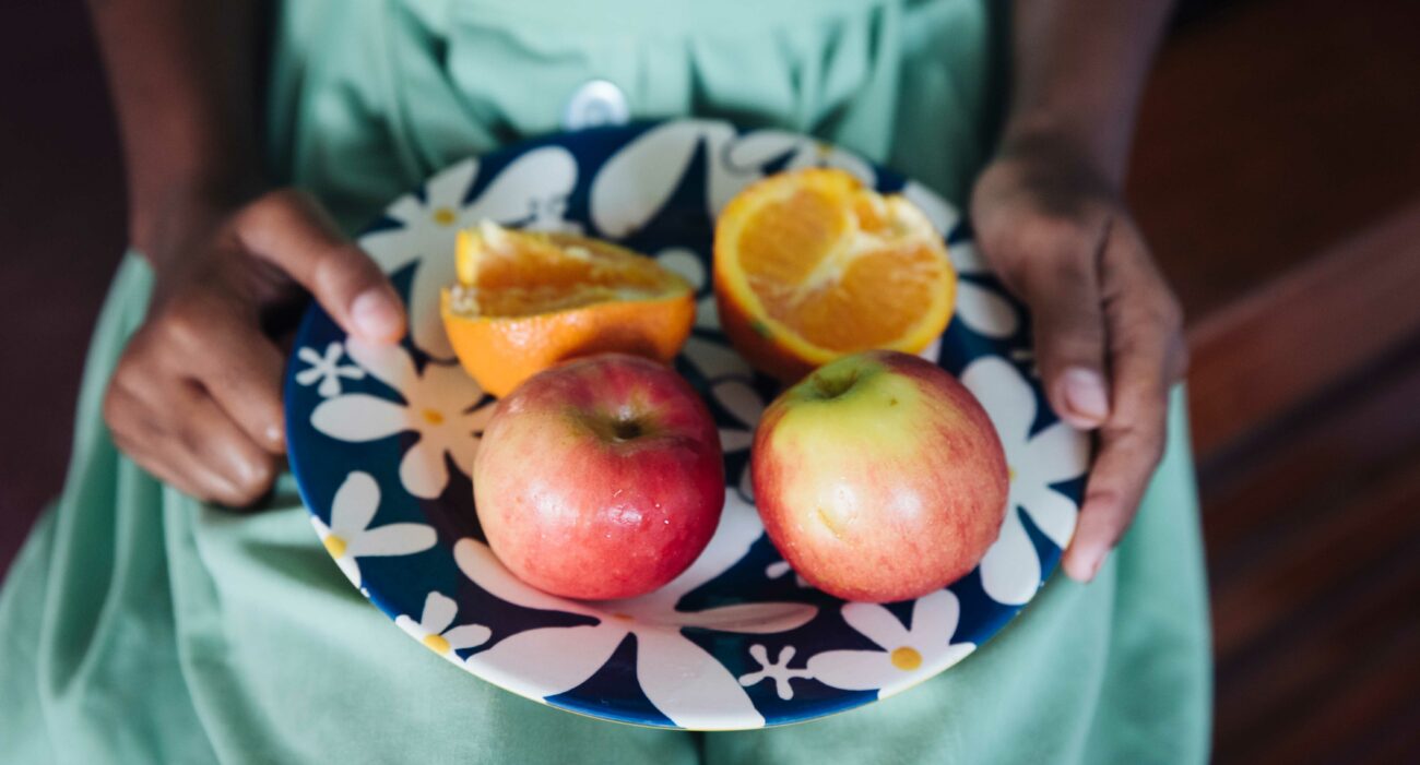 A Fijian school student holds a plate of apples and cut oranges.