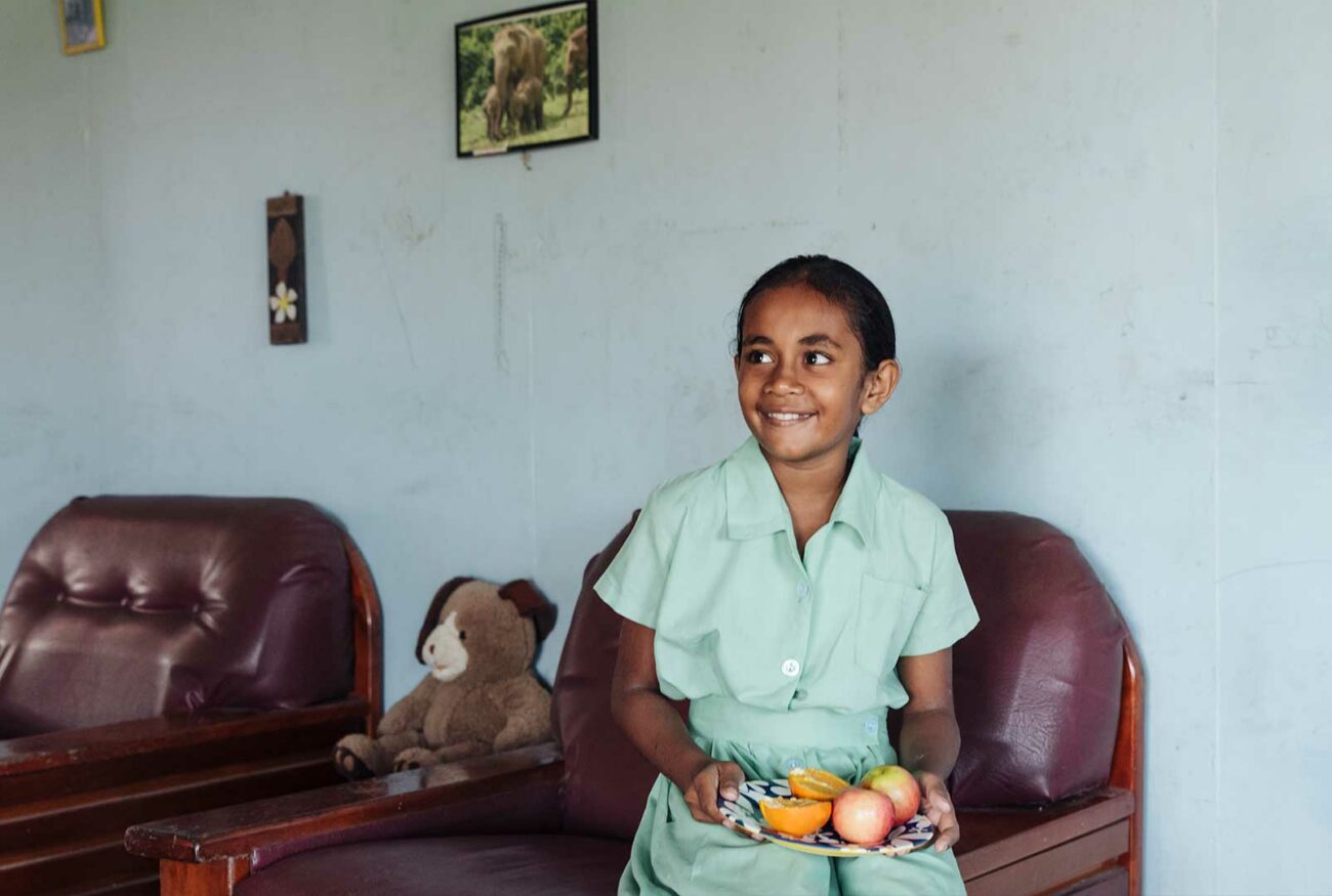 Fijian student who participated in Beyond the Stars sits in her home holding a plate of fruits.