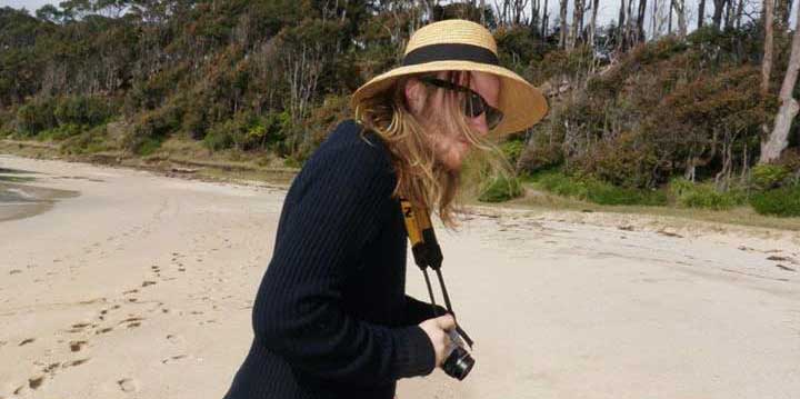 Jack Condon stands on a beach holding a camera.